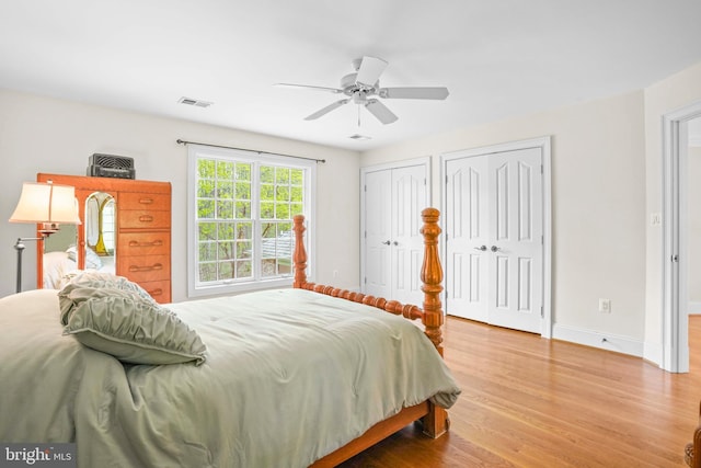 bedroom featuring a ceiling fan, wood finished floors, multiple closets, baseboards, and visible vents