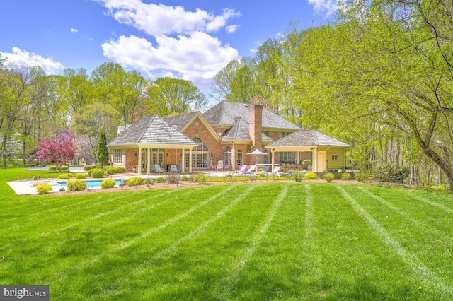 rear view of property featuring a lawn, a chimney, an outdoor pool, and a patio