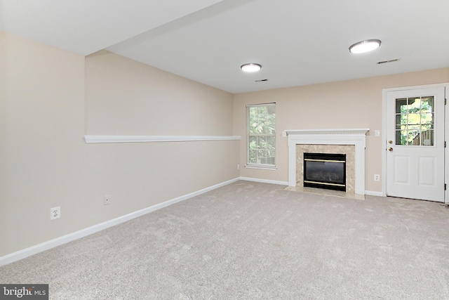unfurnished living room featuring a high end fireplace, baseboards, carpet flooring, and visible vents