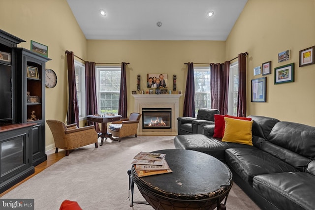 living area featuring a wealth of natural light, vaulted ceiling, carpet, and a glass covered fireplace