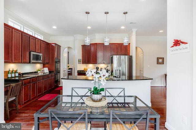 kitchen featuring dark countertops, dark brown cabinets, arched walkways, appliances with stainless steel finishes, and dark wood-type flooring