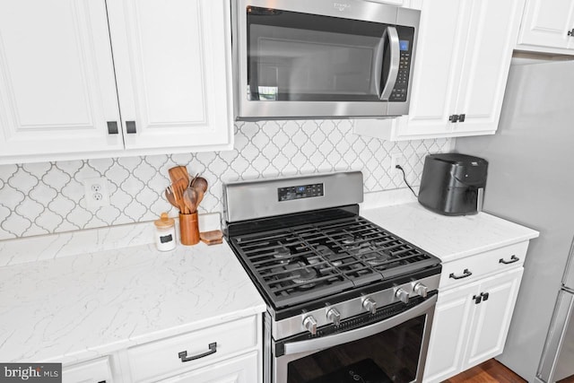 kitchen with white cabinets, light stone countertops, appliances with stainless steel finishes, and decorative backsplash
