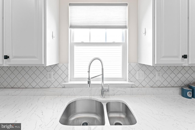 kitchen featuring white cabinetry, light stone countertops, and a sink