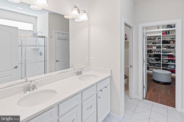 bathroom with double vanity, a sink, a walk in closet, and a stall shower