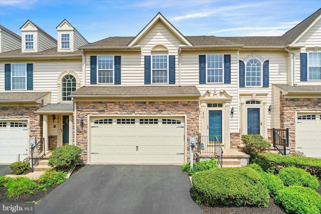townhome / multi-family property with stone siding, aphalt driveway, a shingled roof, and an attached garage