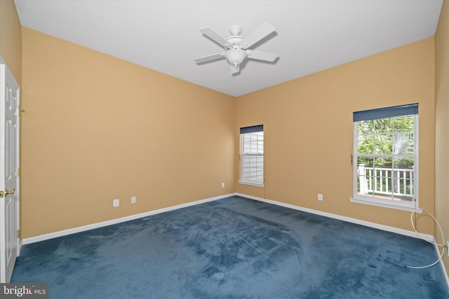 empty room with dark colored carpet, a ceiling fan, and baseboards