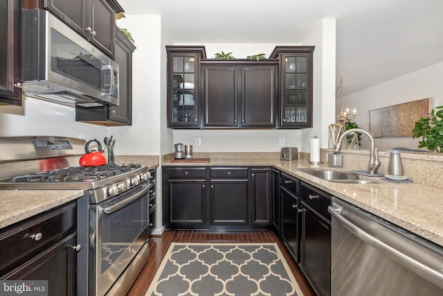 kitchen with light stone counters, stainless steel appliances, glass insert cabinets, and dark wood-style floors