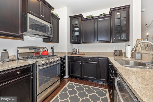 kitchen with light stone counters, glass insert cabinets, a sink, stainless steel appliances, and dark wood-style flooring