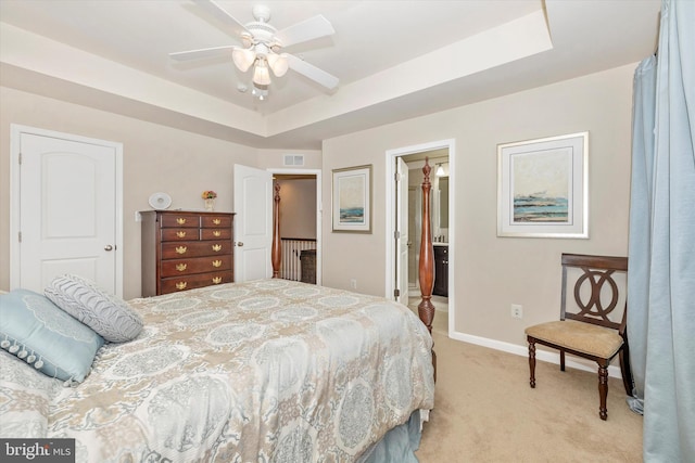 bedroom with connected bathroom, a tray ceiling, visible vents, light carpet, and baseboards