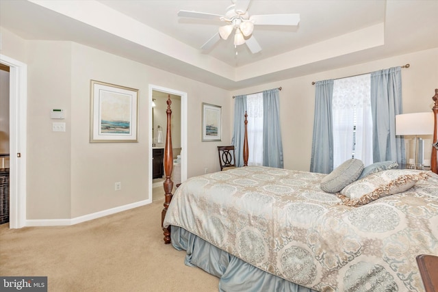 bedroom with baseboards, a raised ceiling, light colored carpet, and ensuite bathroom