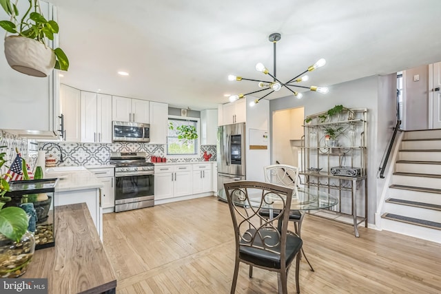 kitchen featuring light countertops, a chandelier, stainless steel appliances, white cabinetry, and decorative backsplash