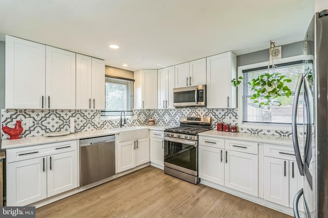 kitchen with a sink, stainless steel appliances, light wood finished floors, and white cabinetry
