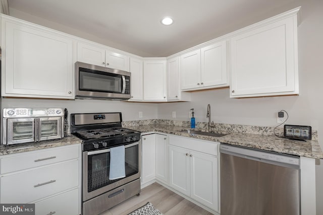 kitchen with a sink, white cabinetry, light stone counters, and stainless steel appliances