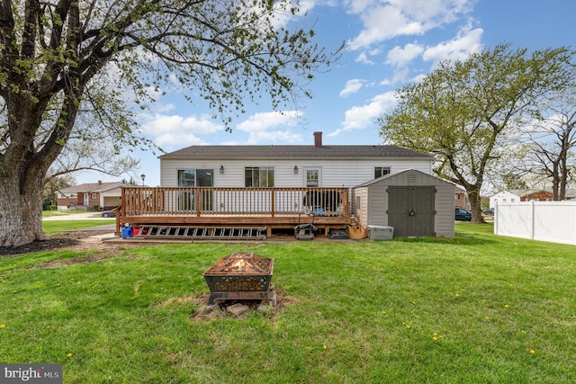 back of property with an outbuilding, a wooden deck, an outdoor fire pit, a storage unit, and fence