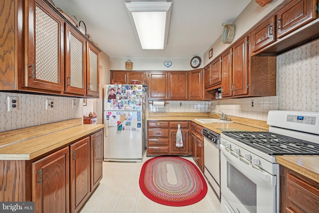 kitchen featuring white appliances, a sink, decorative backsplash, brown cabinets, and wallpapered walls