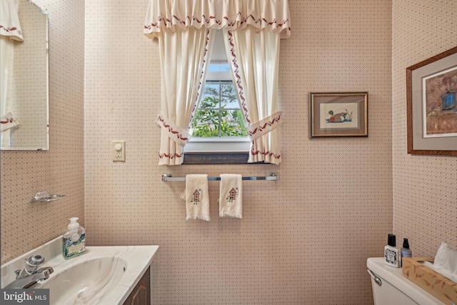 half bathroom with toilet, vanity, and wallpapered walls