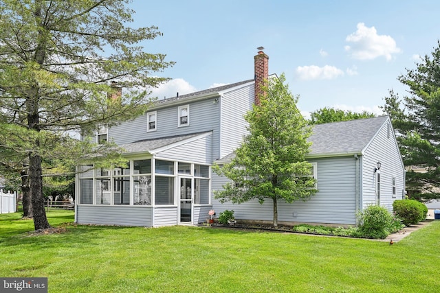 rear view of house with a sunroom, a shingled roof, a yard, and a chimney