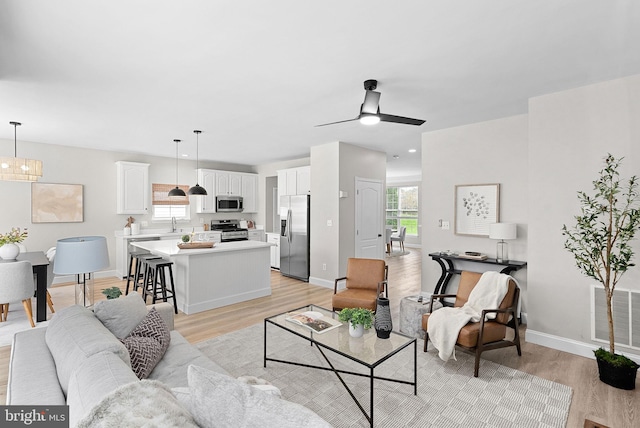 living room with visible vents, ceiling fan, light wood-type flooring, and baseboards