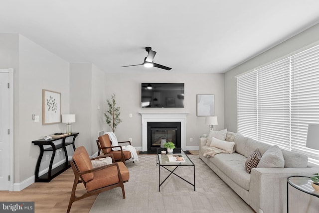 living room with a fireplace with flush hearth, light wood-style floors, ceiling fan, and baseboards