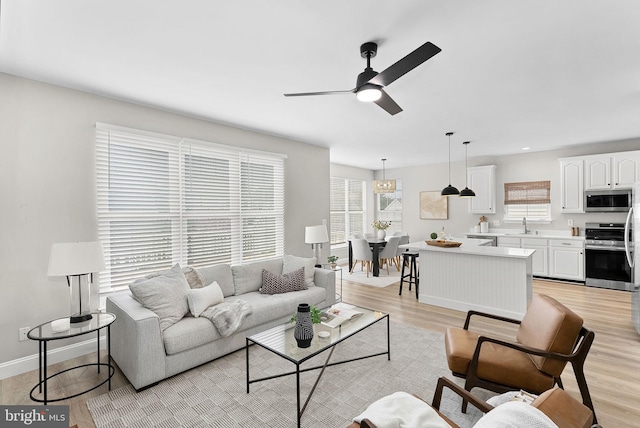 living area with a wealth of natural light, light wood-style flooring, baseboards, and a ceiling fan