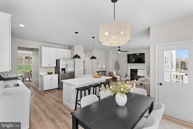 dining space featuring ceiling fan, light wood-style floors, a glass covered fireplace, and baseboards
