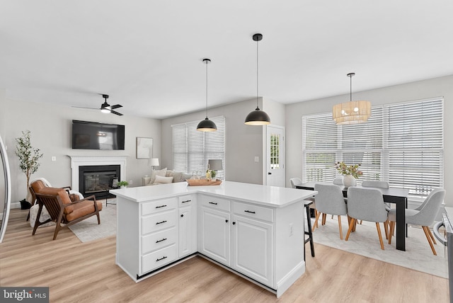 kitchen featuring light countertops, ceiling fan, light wood-type flooring, and a glass covered fireplace