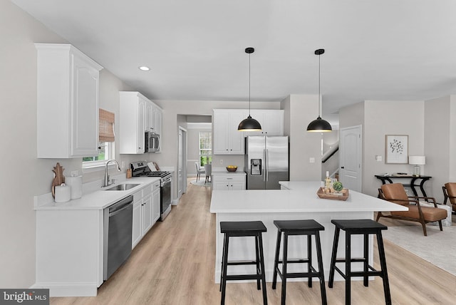 kitchen with white cabinets, a sink, appliances with stainless steel finishes, a kitchen breakfast bar, and light wood-style flooring