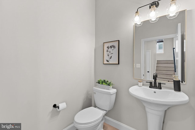 half bathroom with toilet, a sink, and baseboards