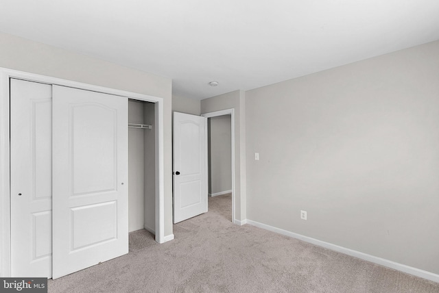 unfurnished bedroom with light carpet, baseboards, and a closet