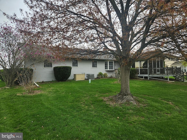 rear view of house with central AC unit, a sunroom, and a lawn