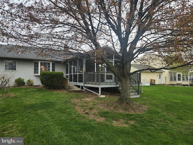rear view of property with a wooden deck, a sunroom, and a lawn
