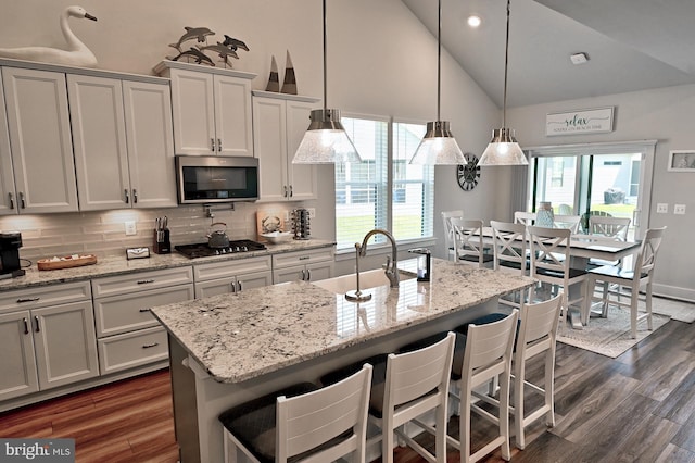 kitchen with high vaulted ceiling, decorative backsplash, stainless steel microwave, and dark wood finished floors