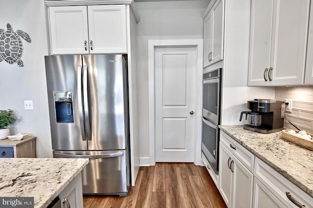kitchen featuring stainless steel appliances, light stone counters, white cabinetry, and wood finished floors