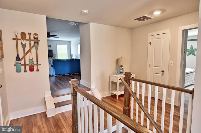 hall featuring baseboards, visible vents, wood finished floors, and an upstairs landing