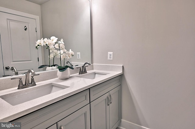 full bath featuring double vanity, a sink, and baseboards