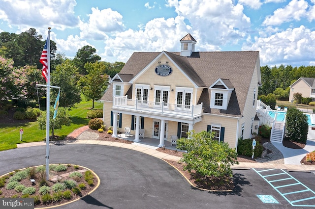 view of front facade featuring a porch, french doors, roof with shingles, uncovered parking, and a balcony