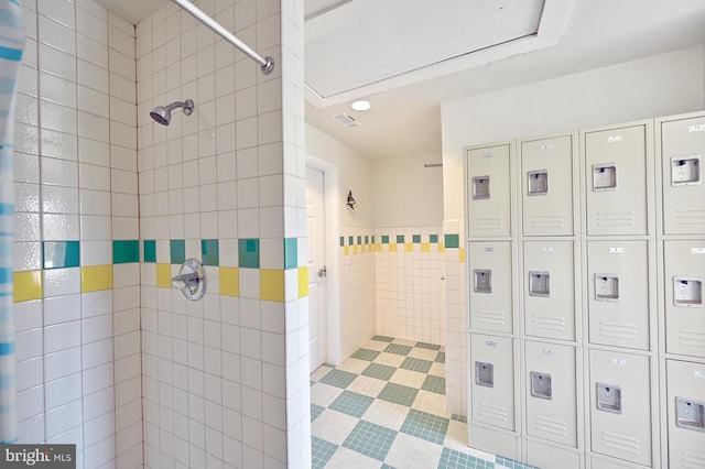 full bath featuring tile patterned flooring, visible vents, a tile shower, and tile walls