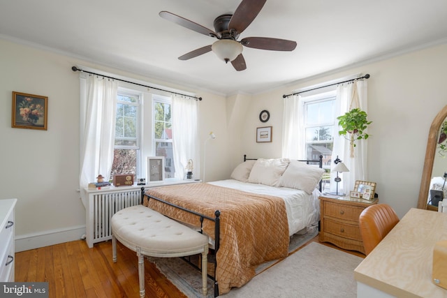 bedroom featuring radiator heating unit, a ceiling fan, ornamental molding, light wood-style floors, and baseboards