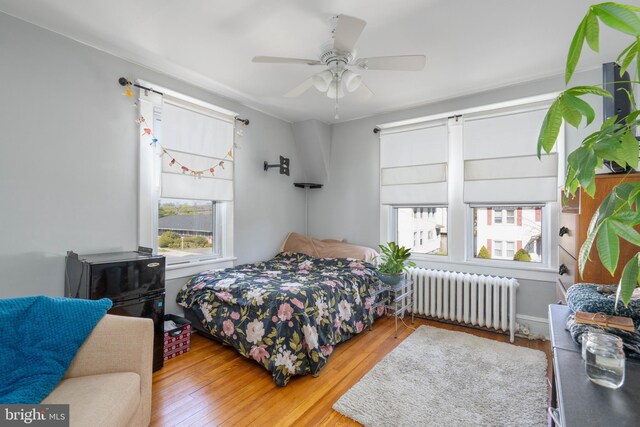 bedroom with multiple windows, wood-type flooring, and radiator