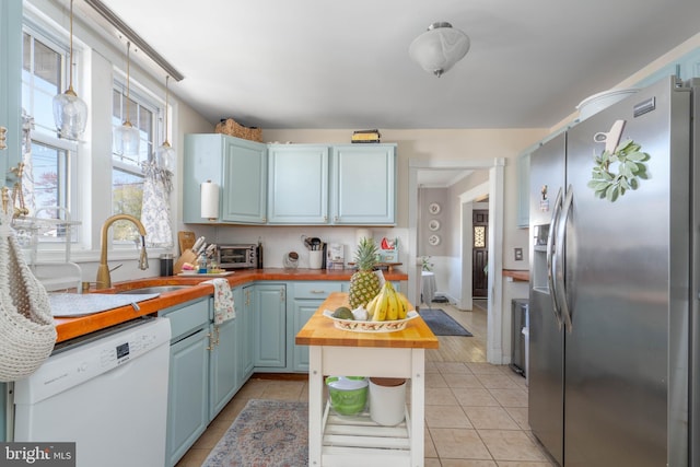 kitchen featuring wooden counters, dishwasher, blue cabinets, a sink, and stainless steel refrigerator with ice dispenser