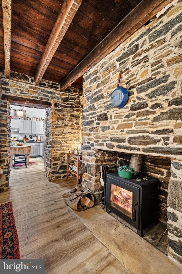 unfurnished living room featuring beamed ceiling, wood finished floors, a wood stove, and wooden ceiling