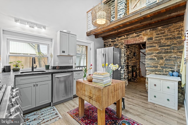 kitchen with a sink, light wood-style floors, appliances with stainless steel finishes, gray cabinetry, and beam ceiling