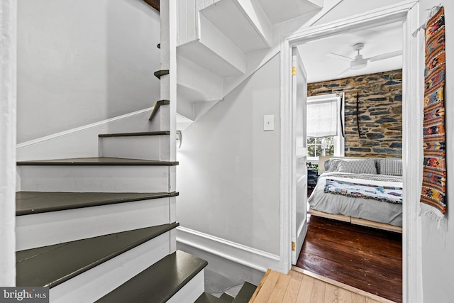 stairs featuring wood finished floors, a ceiling fan, and baseboards