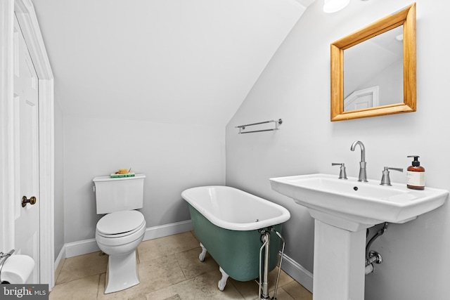 bathroom with vaulted ceiling, a soaking tub, toilet, and baseboards