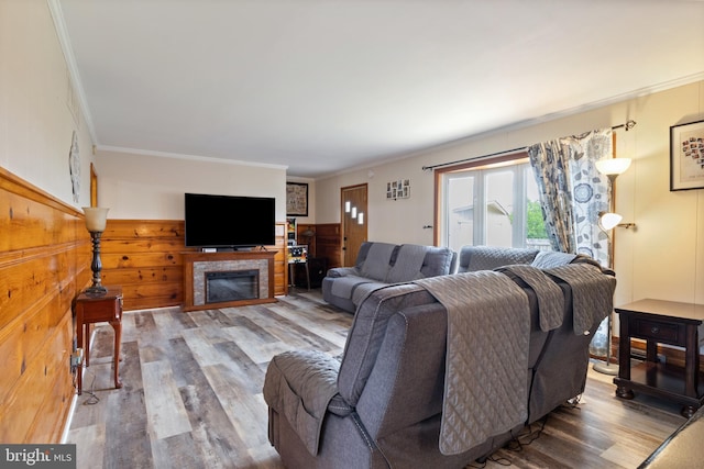 living room with wainscoting, a tiled fireplace, wood finished floors, and ornamental molding
