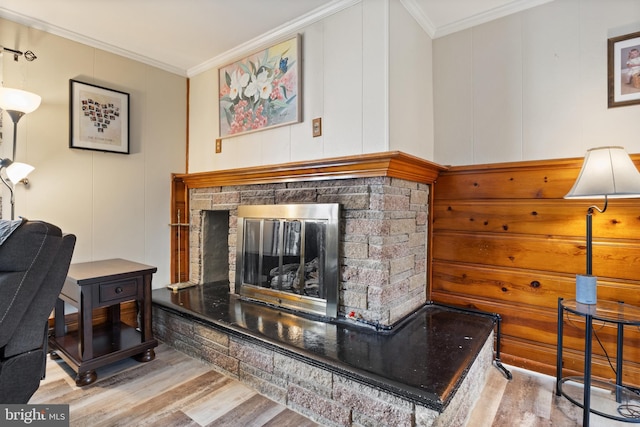 living area with a decorative wall, crown molding, wood finished floors, and a fireplace