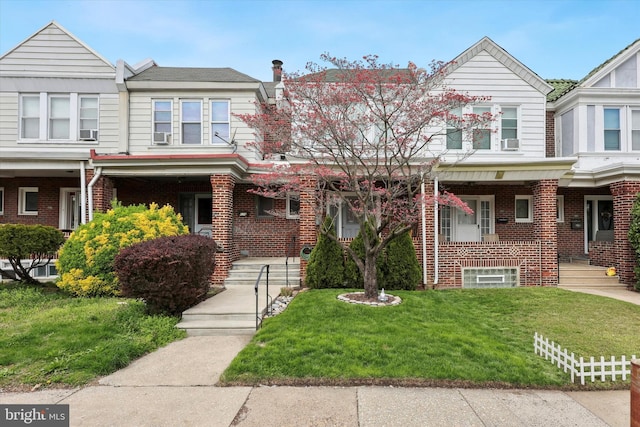 multi unit property with brick siding, a porch, cooling unit, and a front lawn