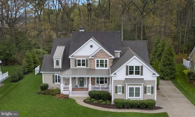 view of front of house featuring board and batten siding, a standing seam roof, a porch, roof with shingles, and a front lawn