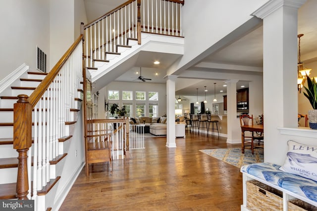 entryway with a high ceiling, a ceiling fan, visible vents, decorative columns, and wood finished floors