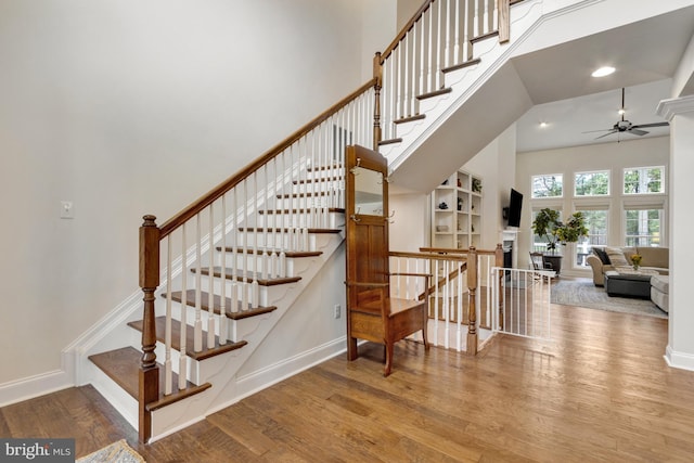 stairs featuring a ceiling fan, recessed lighting, wood finished floors, a high ceiling, and baseboards